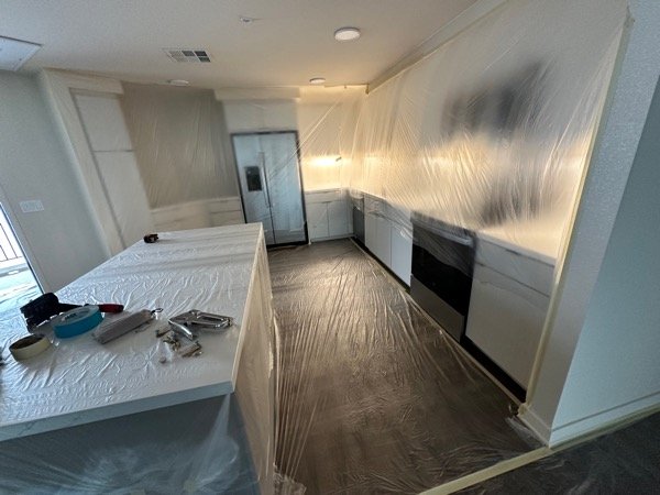 Kitchen with existing flooring and quartz island protected while ceiling grid and ductwork are exposed above