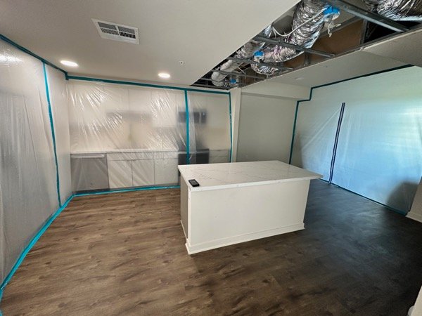 Wide view of kitchen with exposed ceiling framing and sealed cabinetry