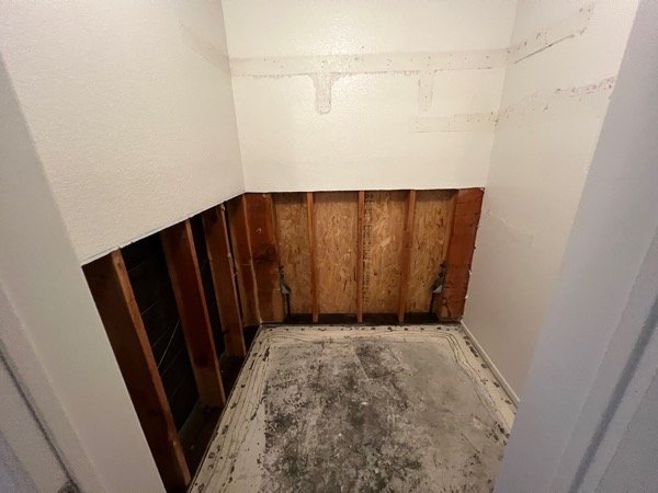 Small room stripped down to wood studs with damaged concrete floor