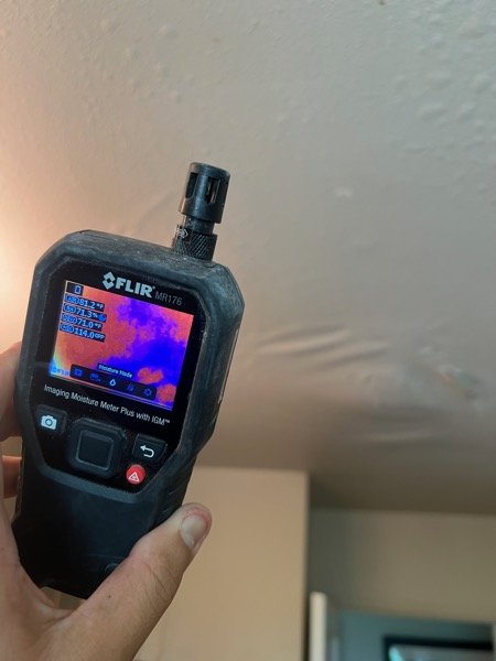 Thermal moisture meter reading a hallway ceiling with visible discoloration