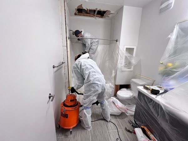 Two Agee Restoration technicians in PPE performing mitigation work in a bathroom